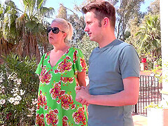 A mature woman with glasses, Maggie Moon, has fun with a young man outdoors.